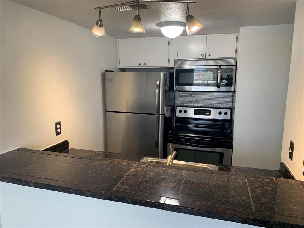 Kitchen featuring a tile-surfaced breakfast bar, stainless steel appliances, stacked-tile backsplash, white cabinetry, and multi-light track fixture
