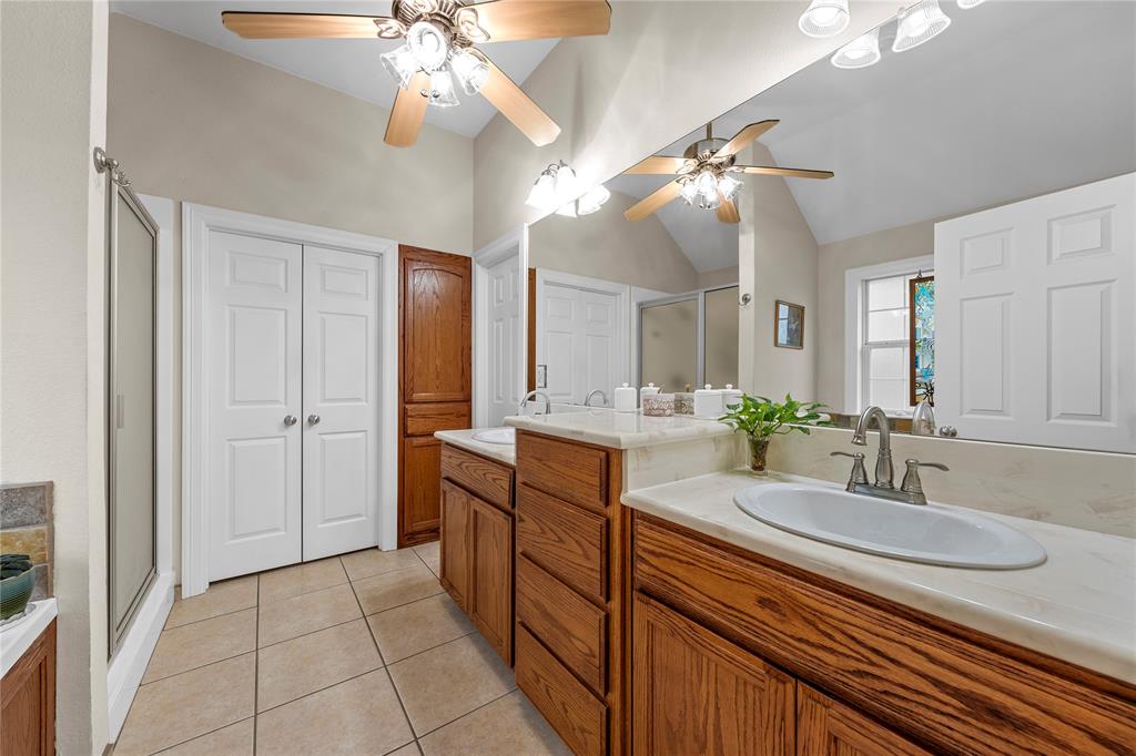 Dual-sink vanity with light-tone countertops, wood cabinetry, tile flooring, and large wall-mounted mirror