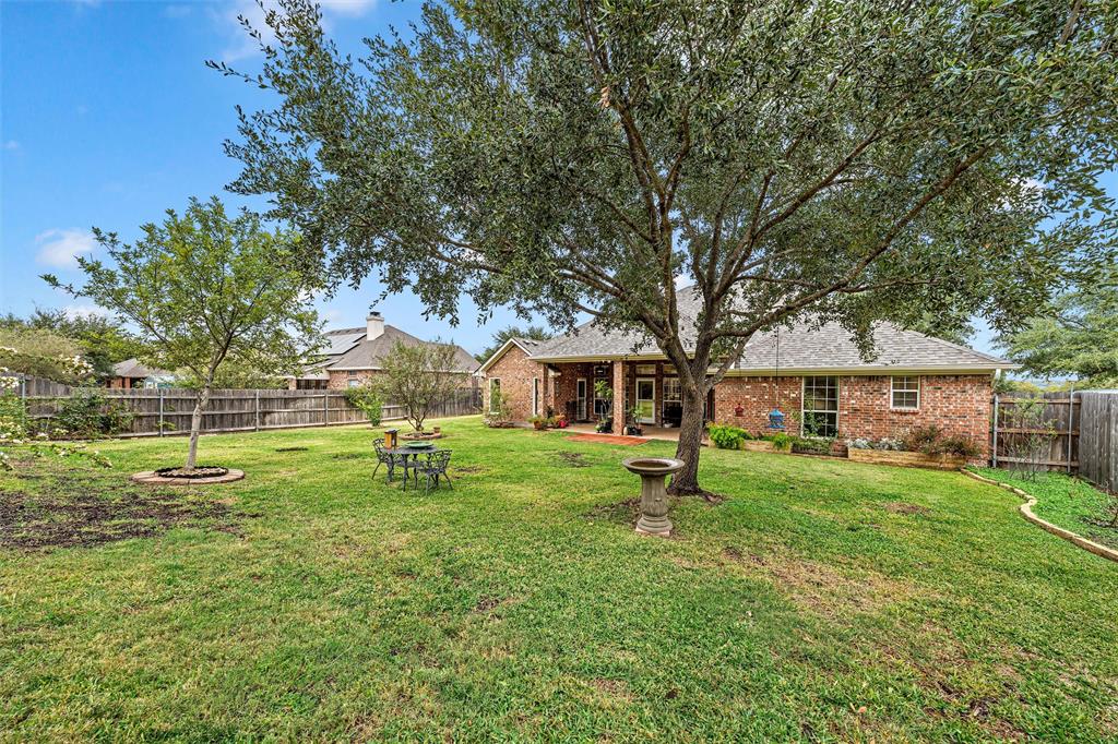 Expansive backyard featuring a brick exterior, covered patio, mature trees, and wood privacy fencing