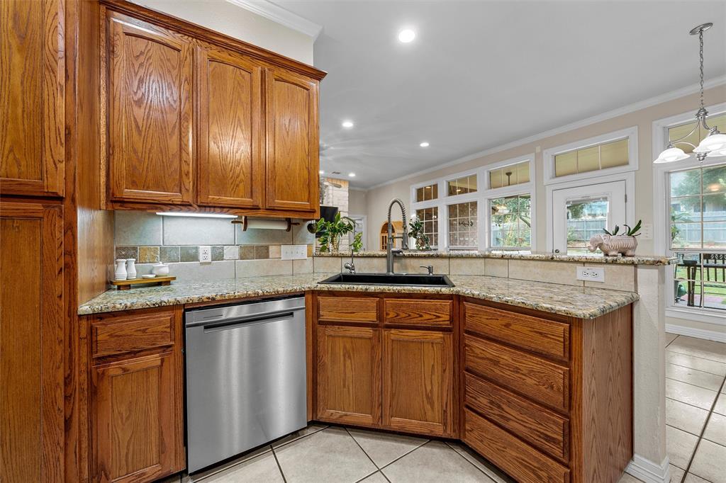 Kitchen featuring stained wood cabinetry, stone-surface countertops, multi-tonal tile backsplash, stainless steel dishwasher, and a dark-finish drop-in sink with a high-arch faucet
