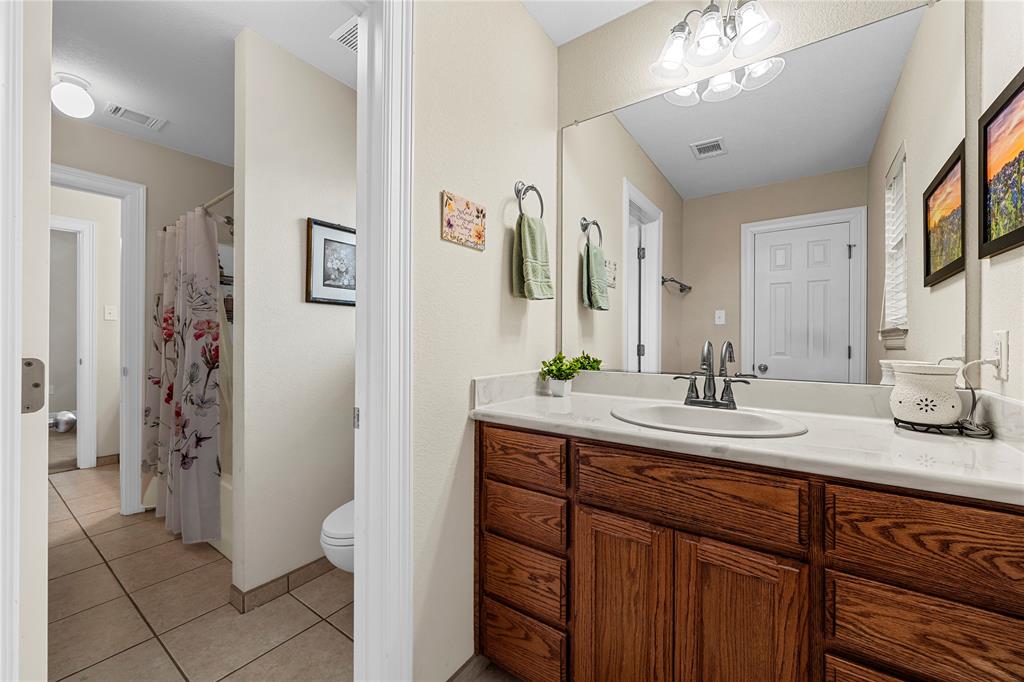Full-width vanity with wood-finish cabinetry, countertop with an integrated oval sink, three-light wall-mounted fixture, and a large plate-glass mirror