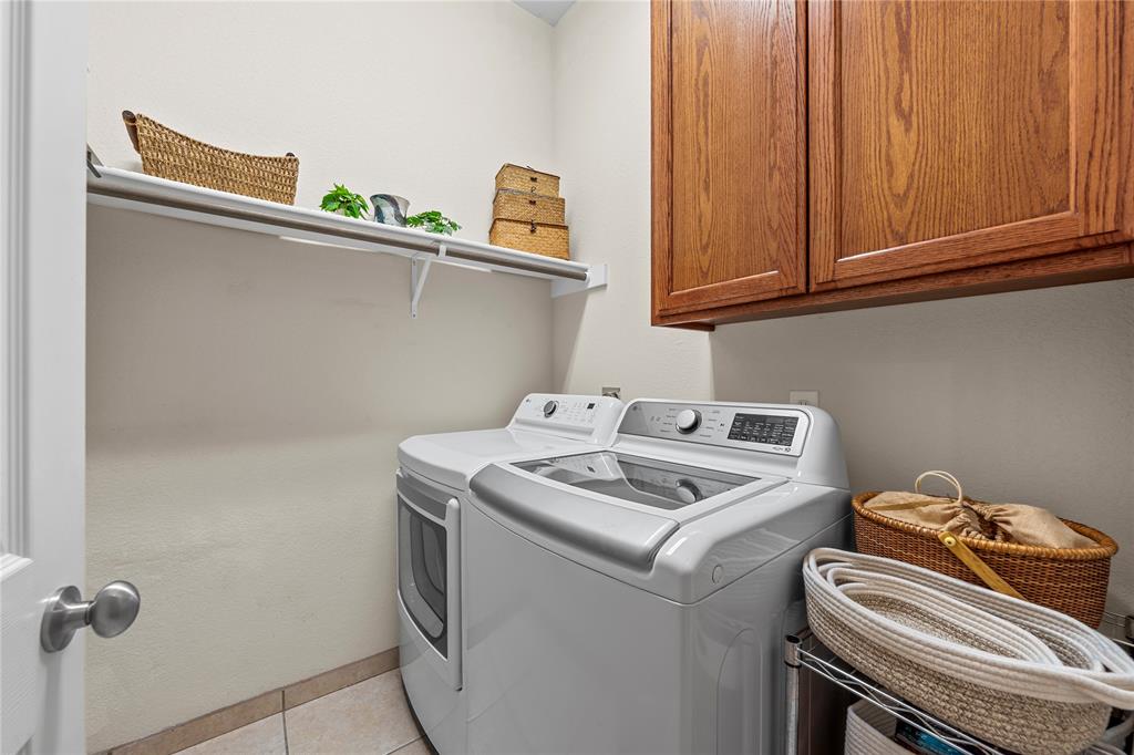 Laundry room featuring natural wood-finish cabinetry, a wide overhead shelf, and tile flooring