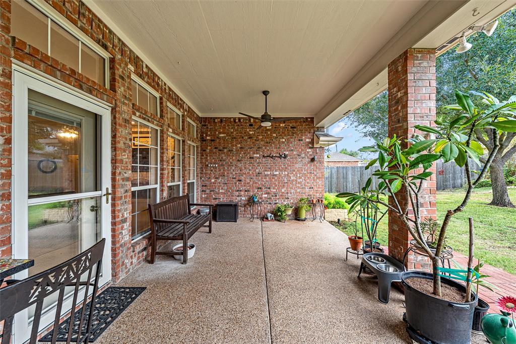Covered patio featuring exposed brick exterior walls, a concrete floor, integrated ceiling fan, and large windows with transom accents