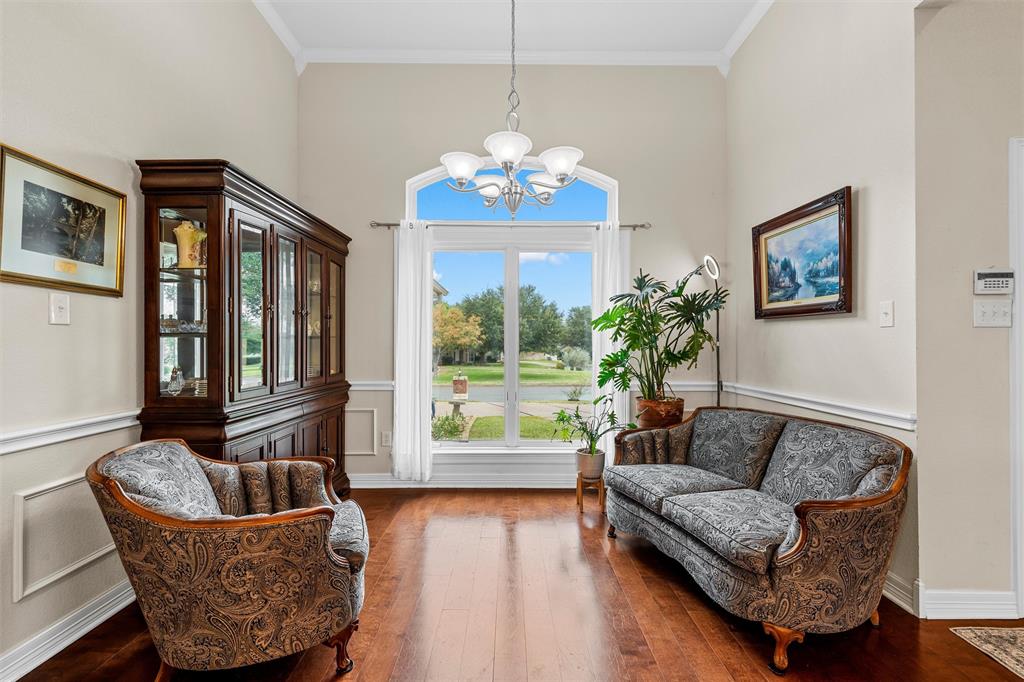 High-ceilinged room featuring wood-finish flooring, wainscoting, a multi-light chandelier, and an arched window High-ceilinged room featuring wood-finish flooring, wainscoting, a multi-light chandelier, and an arched window