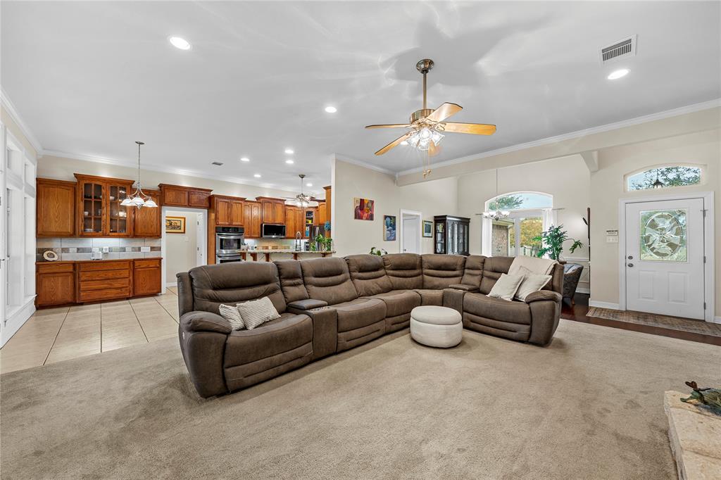 Open-concept interior featuring light-toned carpeting, recessed lighting, ceiling fans with integrated light fixtures, kitchen with wood cabinetry, and an exterior door with decorative glass paneling Open-concept interior featuring light-toned carpeting, recessed lighting, ceiling fans with integrated light fixtures, kitchen with wood cabinetry, and an exterior door with decorative glass paneling