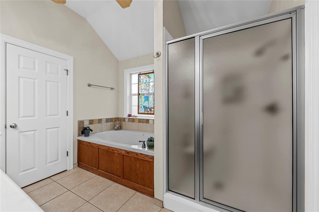 Bathroom featuring a soaking tub with wood-finish paneling, tiled surround, vaulted ceiling, and an enclosed shower with a metal frame