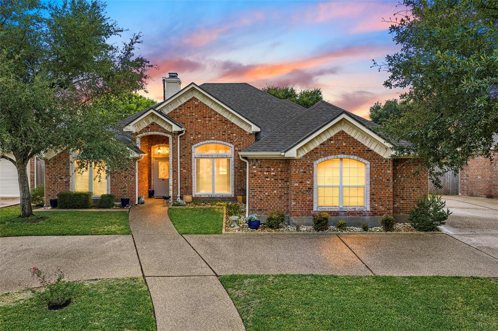 Brick exterior featuring a gabled roofline, arched window detailing, an arched covered entryway, and a paved concrete driveway Brick exterior featuring a gabled roofline, arched window detailing, an arched covered entryway, and a paved concrete driveway