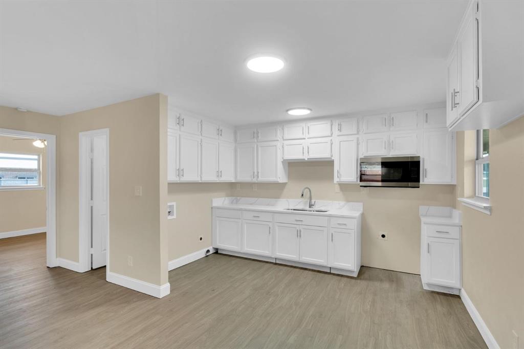 Kitchen featuring white cabinetry, stone-finish countertops, stainless steel microwave, gooseneck faucet, and wood-finish flooring