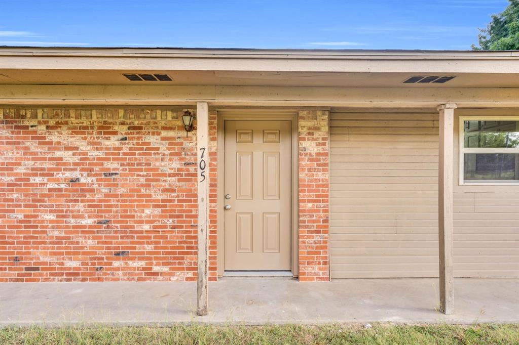 Exterior elevation featuring a red brick facade, a covered front porch with support pillars, and a six-panel entry door Exterior elevation featuring a red brick facade, a covered front porch with support pillars, and a six-panel entry door
