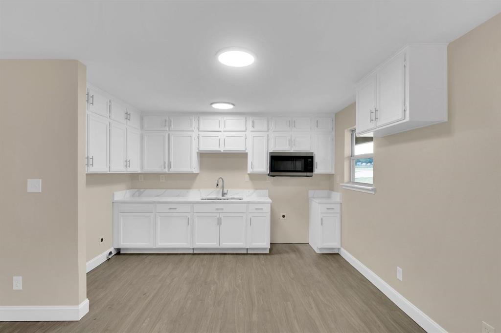 Kitchen featuring white cabinetry, wood-finish flooring, stone-style countertops, an undermount sink, and a built-in microwave