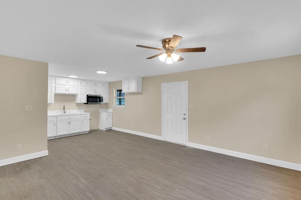 Kitchen area featuring white cabinetry, a built-in microwave, and a sink, complemented by wood-finish flooring and an overhead ceiling fan