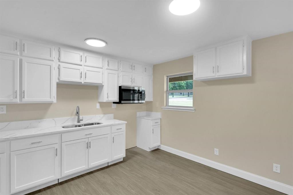 Kitchen featuring white cabinetry, stone-finish countertops, an integrated microwave, a double-basin stainless steel sink with a high-arch faucet, and wood-finish flooring