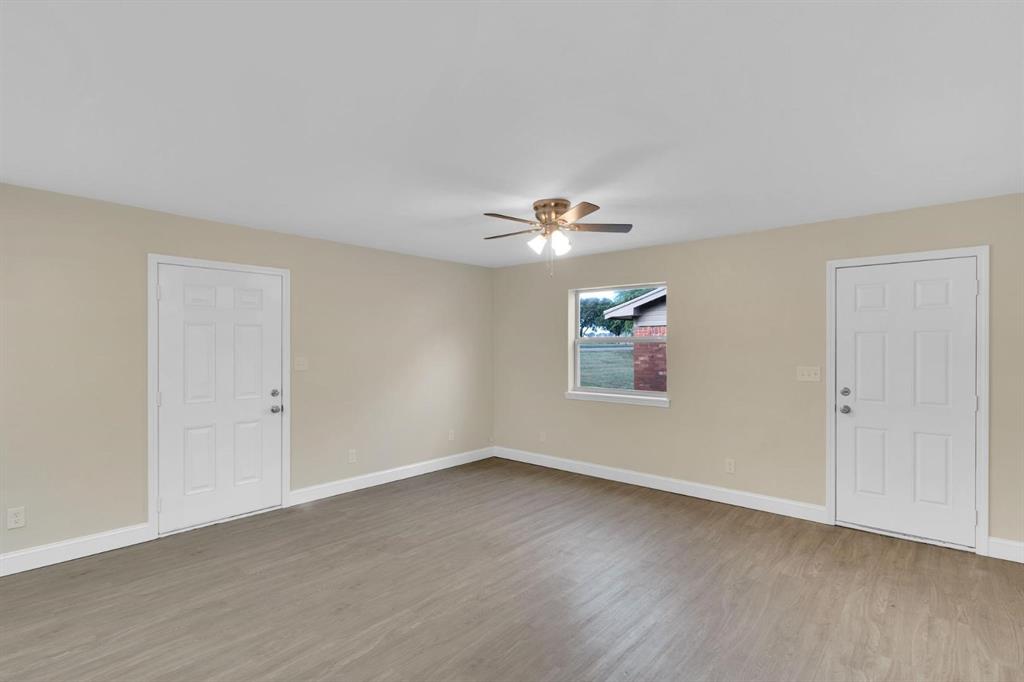 Neutral-toned interior space featuring wood-finish flooring, a ceiling fan with integrated lighting, two six-panel doors, and a single-pane window