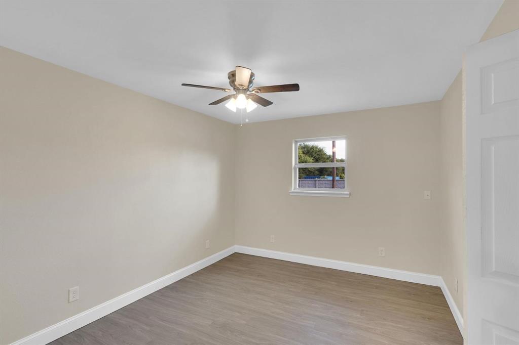 Neutral-toned room featuring wood-finish flooring, a central ceiling fan with integrated lighting, and a single-pane window