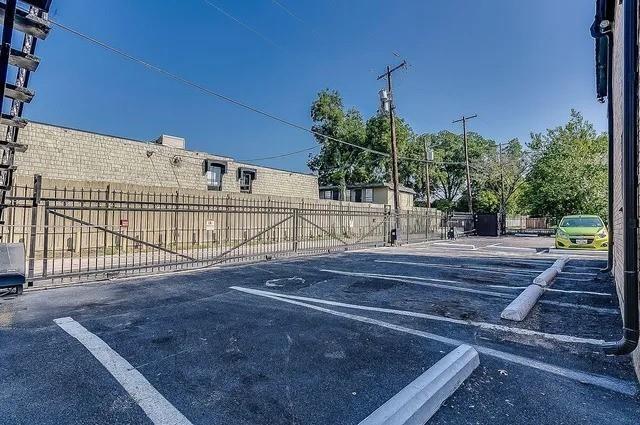 Asphalt parking lot featuring painted stall lines, concrete wheel stops, and a secure metal perimeter fence