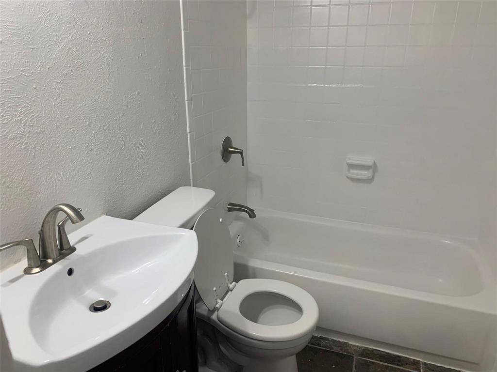 Bathroom featuring a white pedestal sink with a metallic faucet, a porcelain-surround shower and tub combination with a built-in soap dish, and dark tiled flooring