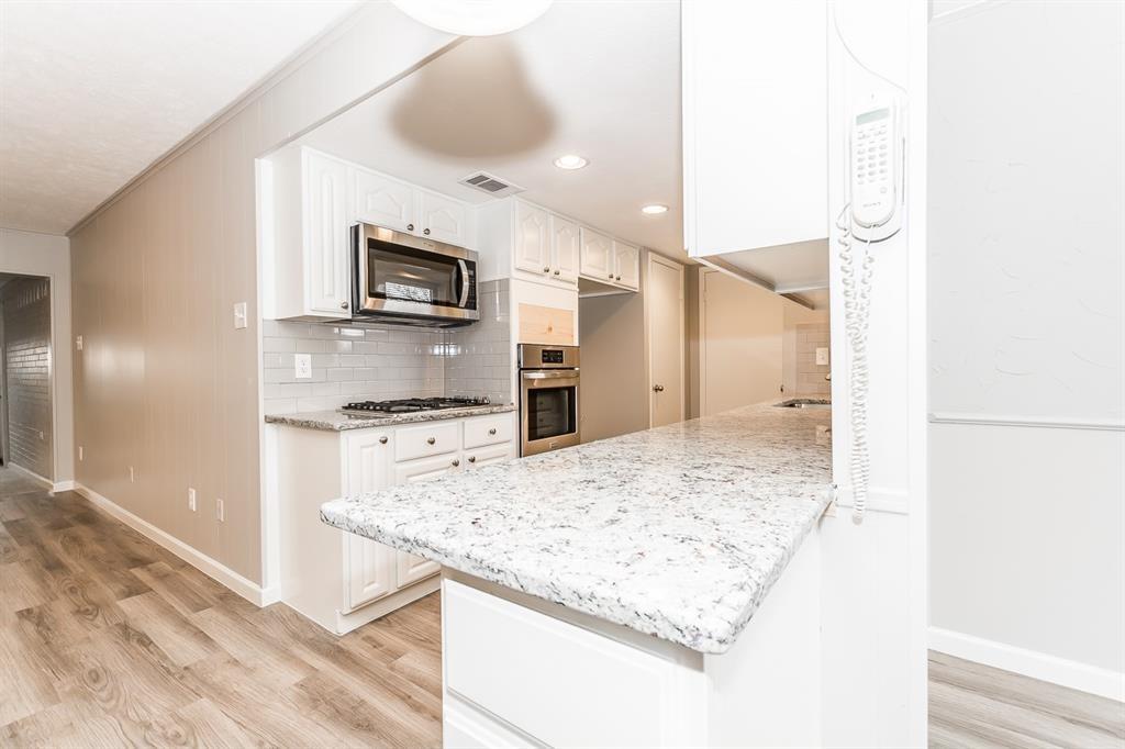 Kitchen featuring white cabinetry, stone-surface countertops, subway tile backsplash, stainless steel built-in microwave, and wood-finish flooring