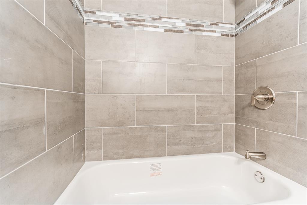 Bathtub surround featuring large-format ceramic tile, a decorative mosaic glass tile accent border, and brushed nickel hardware
