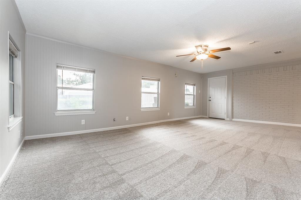 Neutral-toned interior featuring vertical paneled wall treatments, a painted brick accent wall, carpeted flooring, and a ceiling-mounted light fixture with fan blades