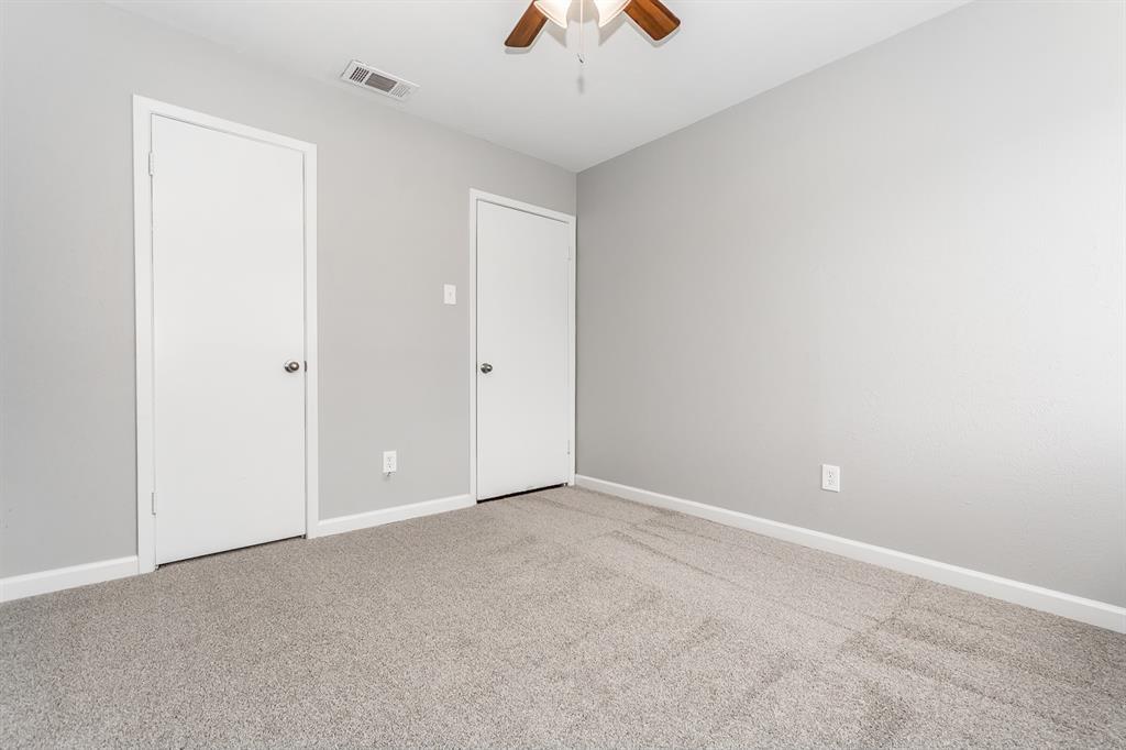Neutral interior room featuring neutral-toned carpeting, two interior doors, and a ceiling fan with integrated lighting