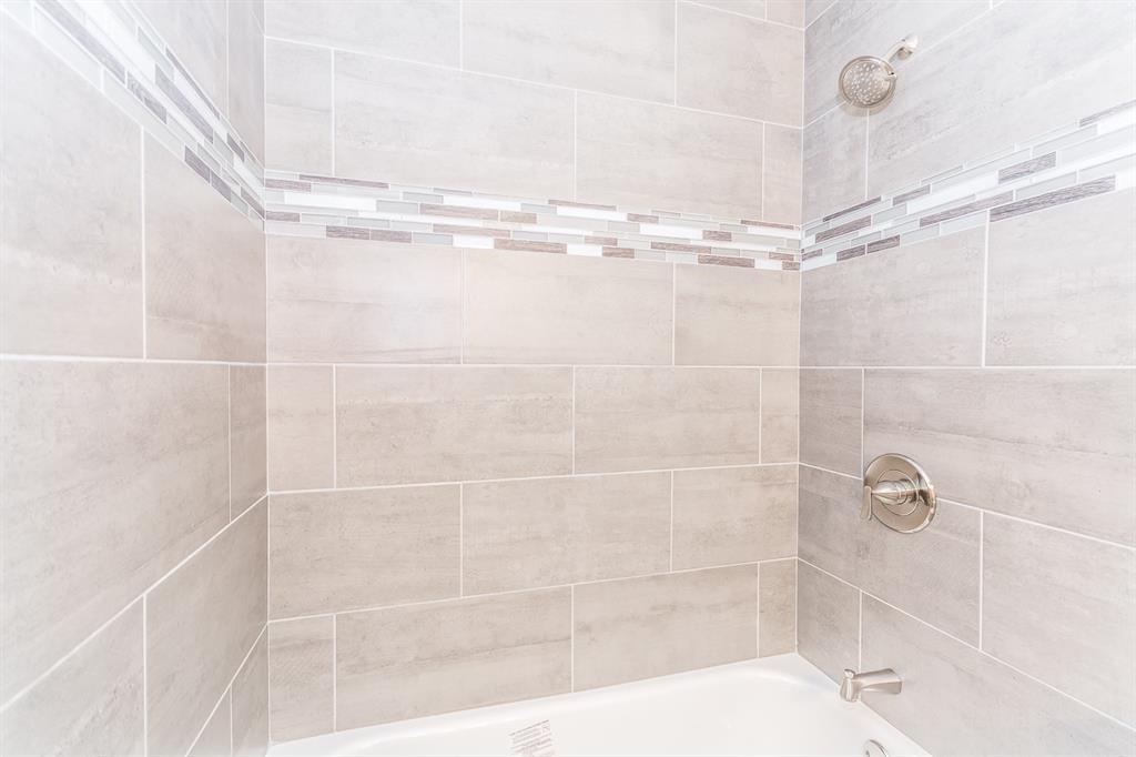 Shower surround featuring large-format neutral-toned tile, decorative glass mosaic accent inlay, polished chrome single-handle pressure balance valve, and a wall-mounted shower head