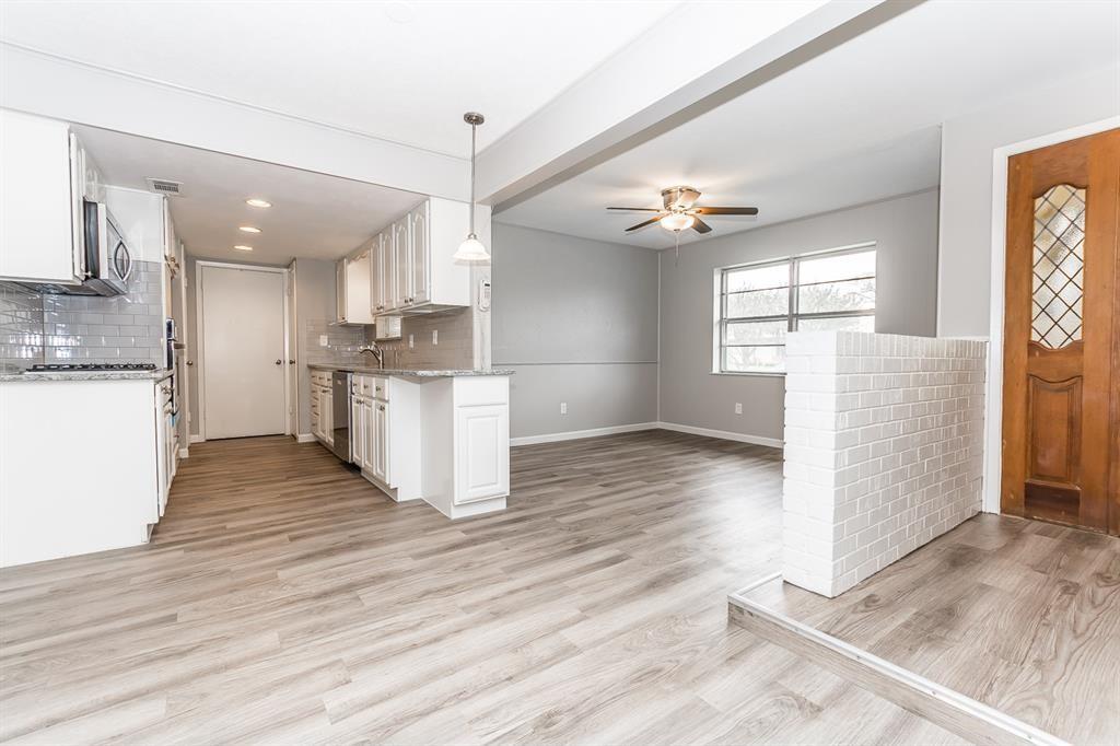 Kitchen featuring white shaker-style cabinetry, stone-surface countertops, subway tile backsplash, wood-finish flooring, and a decorative white brick partial wall