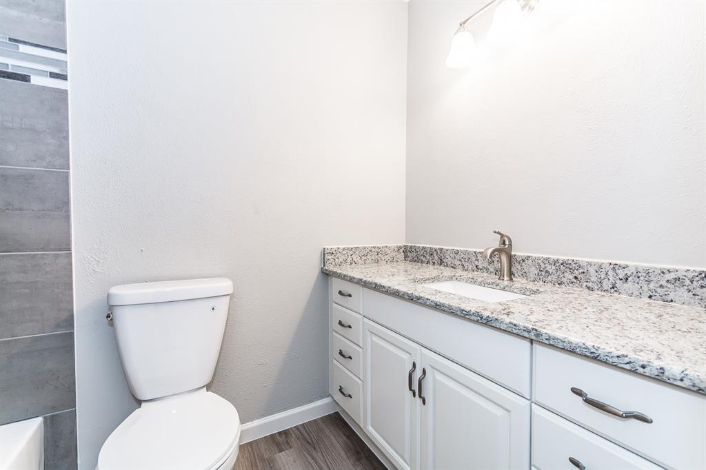 Bathroom vanity featuring white cabinetry, stone-finish countertop, undermount sink, brushed nickel hardware, and wood-finish flooring