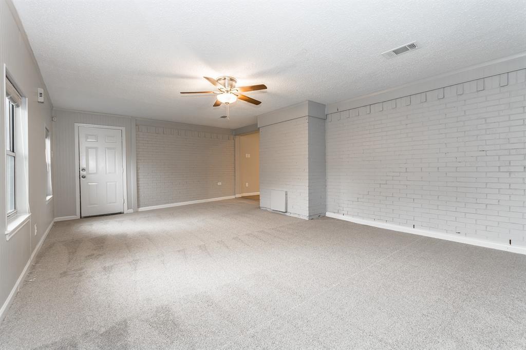 Spacious interior featuring painted brick wall accents, wall-to-wall carpeting, and a ceiling fan with integrated lighting