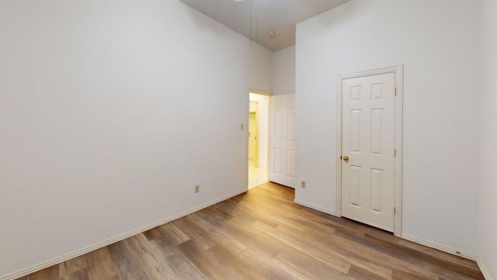 Interior room featuring high ceilings, wood-finish flooring, and a six-panel door Interior room featuring high ceilings, wood-finish flooring, and a six-panel door