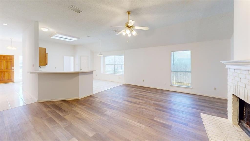 Open-concept living space featuring wood-finish flooring, vaulted ceilings, a brick fireplace, and a breakfast bar