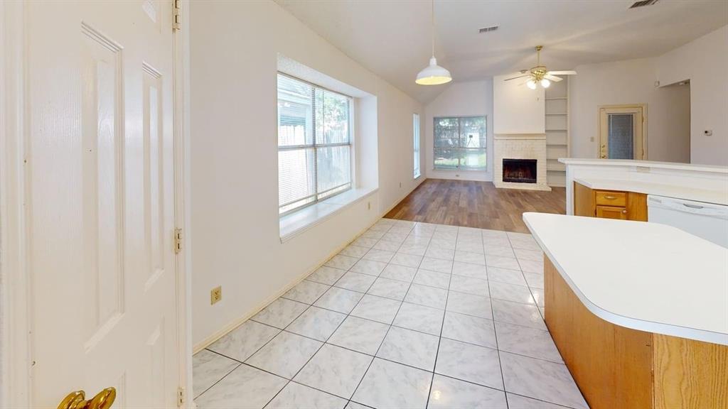 Open-concept interior featuring light tile flooring, wood-finish flooring, a fireplace with integrated shelving, and a peninsula kitchen counter