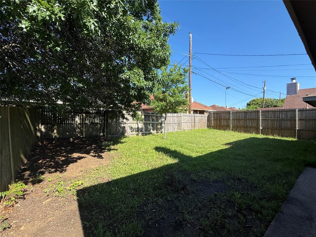 Backyard featuring a grass lawn, perimeter wood fencing, and mature trees
