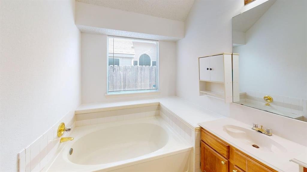 Oval soaking tub, wood-finish cabinetry, integrated vanity sink, wall-mounted medicine cabinet, and large-format wall mirror