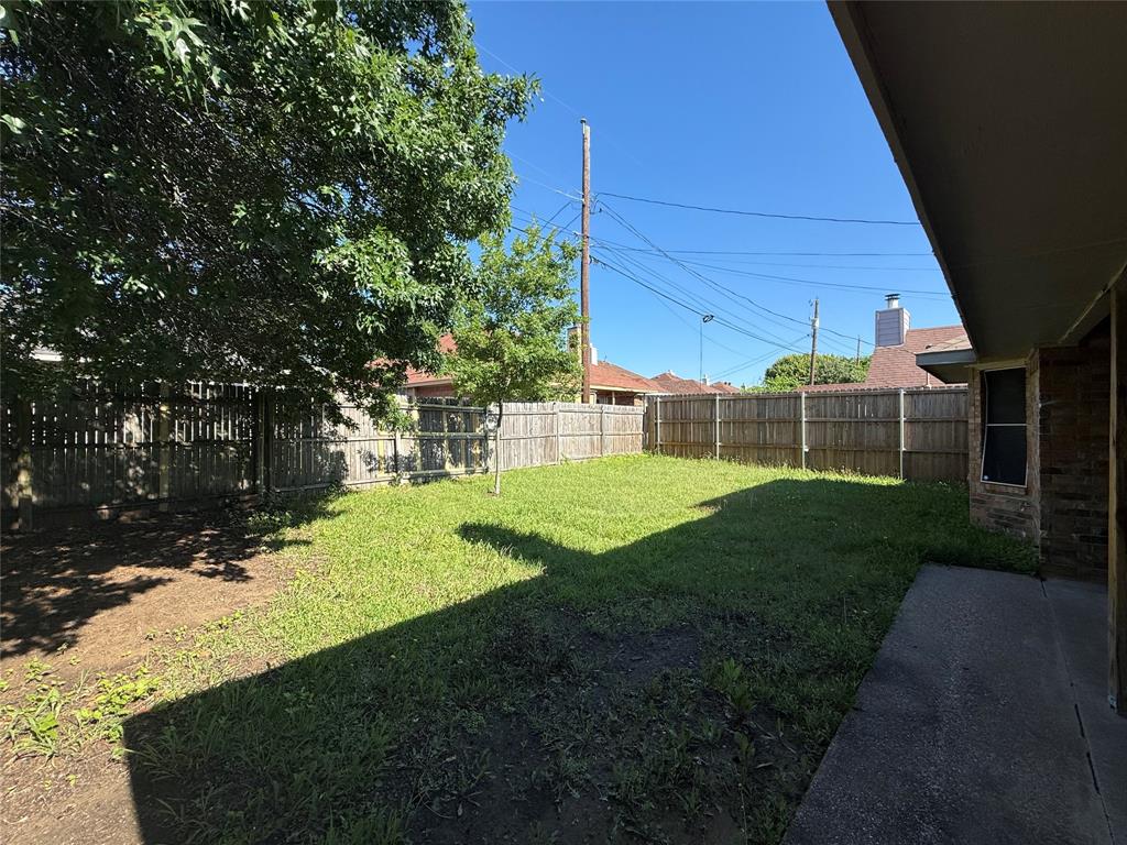 Rear exterior space featuring a concrete patio, wood privacy fencing, grass lawn, and mature trees