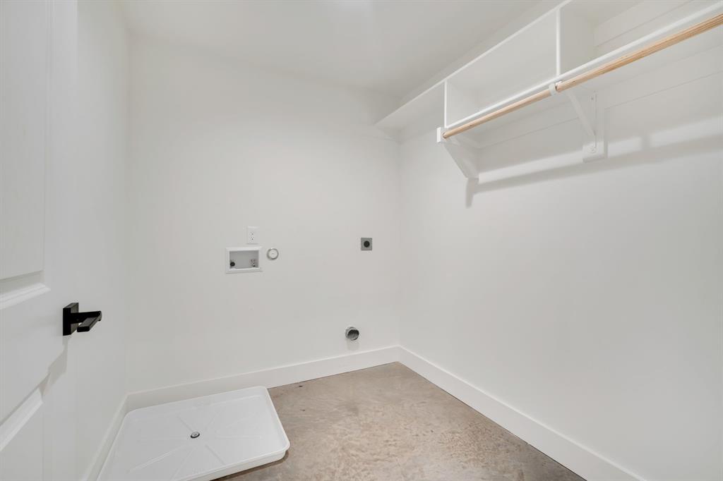 Utility area featuring white built-in shelving, a wooden hanging rod, a white floor-mounted drainage pan, and a black lever-style door handle