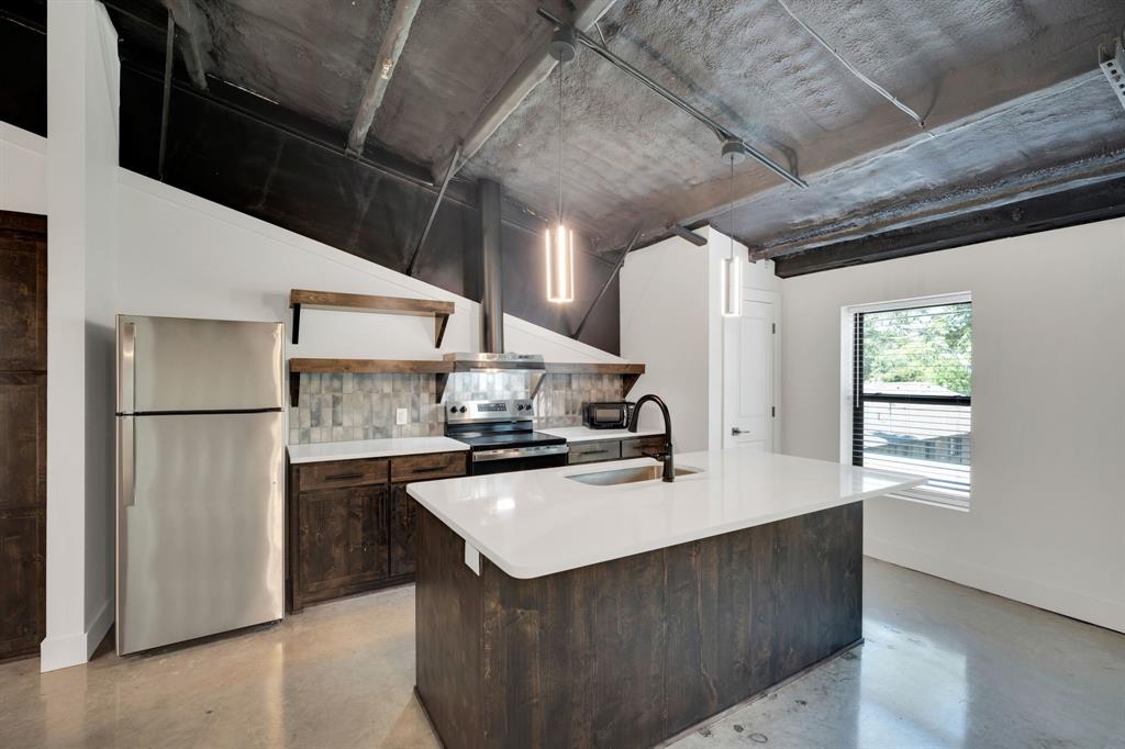 Kitchen featuring stained wood cabinetry, central island with stone-finish countertop, stainless steel appliances, tiled backsplash, and exposed industrial-style ceiling