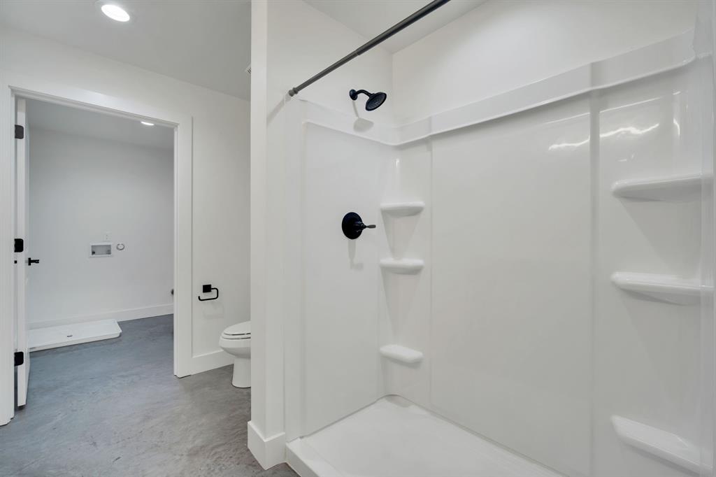 Walk-in shower enclosure with integrated shelving, matte black fixtures, and neutral flooring