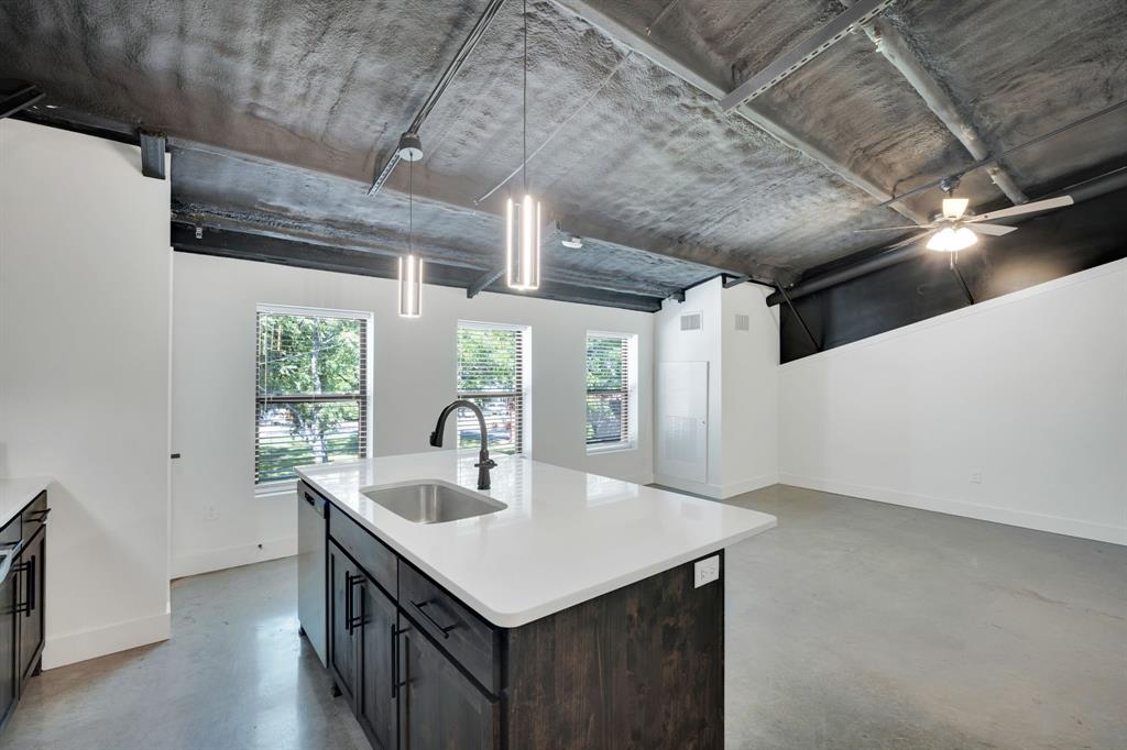 Industrial-style interior featuring exposed concrete ceilings, a kitchen island with stone-surface countertop, dark-finish cabinetry, concrete flooring, and pendant lighting