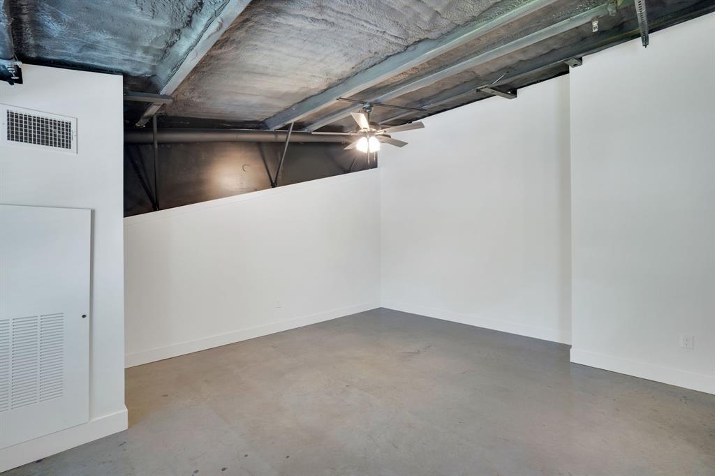 Industrial-style room featuring high exposed ceilings, concrete flooring, crisp white walls, and a center-mounted ceiling fan