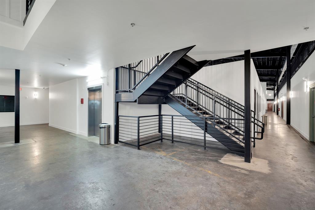 Industrial-style staircase featuring metal treads, horizontal railing, and exposed structural support beams, paired with a stainless steel elevator