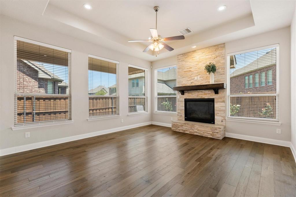 Living area featuring wood-finish flooring, a tray ceiling, recessed lighting, and a floor-to-ceiling stone-surround fireplace with a wooden mantel