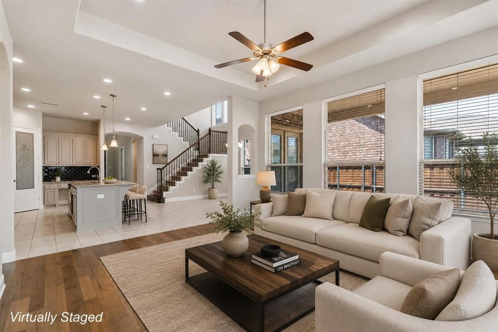 Open-concept interior featuring wood-finish flooring, a tray ceiling with a multi-blade light fixture, recessed lighting, and a kitchen island with a stone-top surface