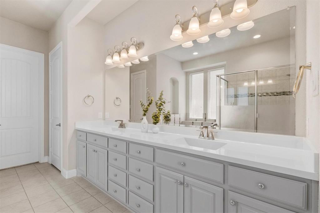 Dual-sink vanity with light-gray cabinetry, expansive countertop, full-width wall mirror, and two multi-bulb overhead light fixtures