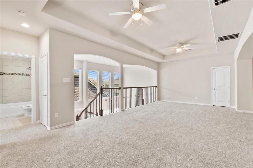 Expansive upper level featuring a tray ceiling, dual ceiling fans, iron balustrade railing, and neutral wall-to-wall carpeting
