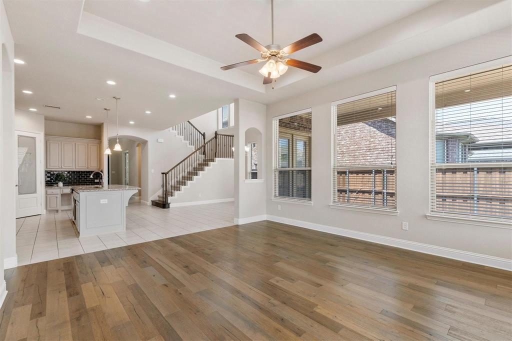 Open-concept interior featuring wood-finish flooring, tray ceilings with a central fan, large windows, a staircase with metal balusters, and a kitchen island with stone countertops