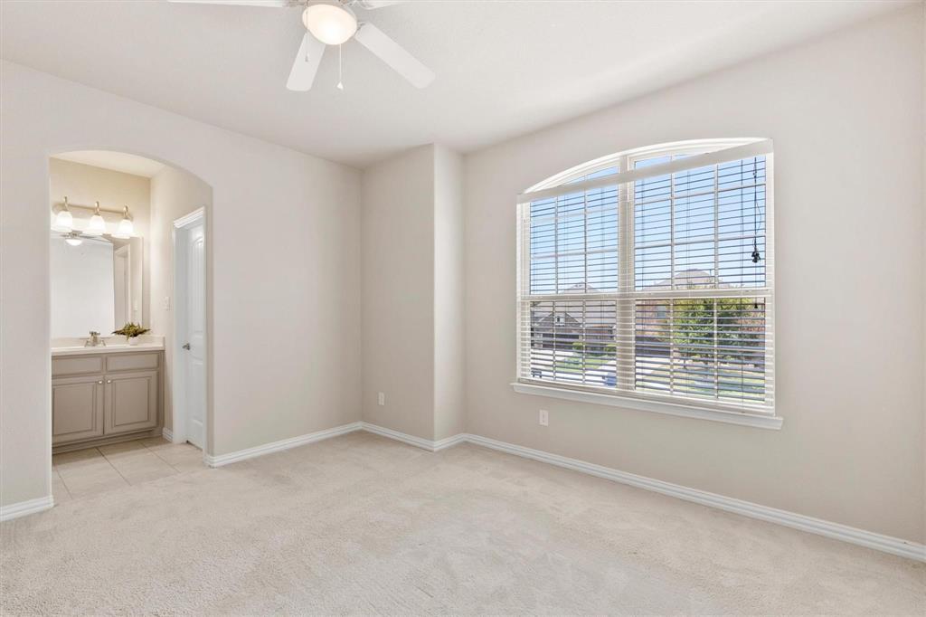 Room featuring neutral wall tones, arched doorway, ceiling fan with light fixture, and a large window with an arched transom