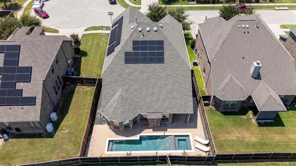 Aerial perspective featuring a multi-faceted shingle roof with integrated solar panels, a fenced backyard, and a rectangular swimming pool with an attached spa