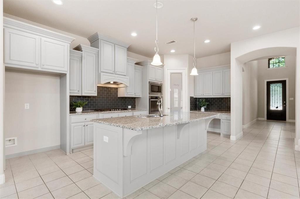 Kitchen featuring light-toned cabinetry, a spacious stone-topped island, dark subway-tile backsplash, built-in double wall ovens, and recessed lighting