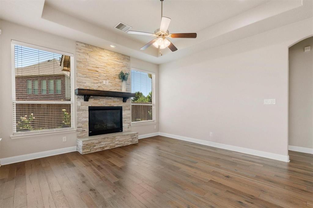 Living area featuring wood-finish flooring, a tray ceiling with a center-mounted ceiling fan, and a floor-to-ceiling stacked stone fireplace with a substantial timber mantel