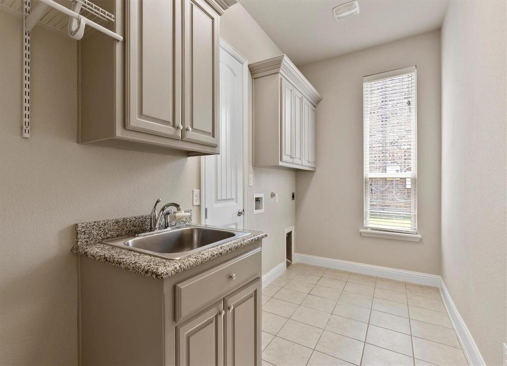 Laundry room featuring tile flooring, stone-finish countertops, stainless steel undermount sink, built-in cabinetry, and a window with horizontal blinds